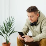 Teenage boy in a hoodie reading his smartphone with headphones around his neck