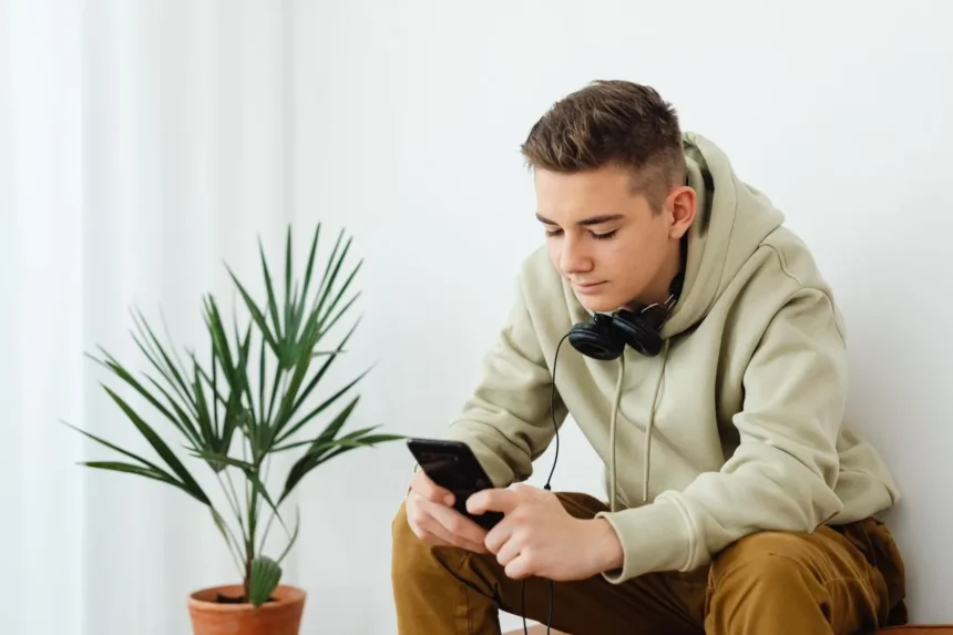 Teenage boy in a hoodie reading his smartphone with headphones around his neck